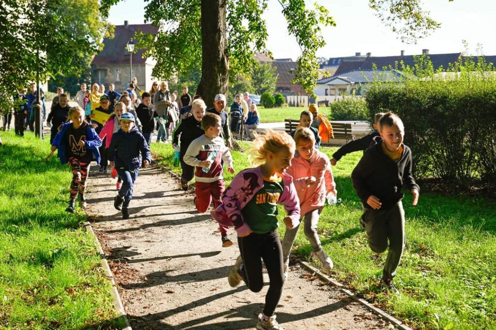 Uczniowie biegną ścieżkami parku, bieg pod hasłem "Kultura zdobi i ułatwia życie".