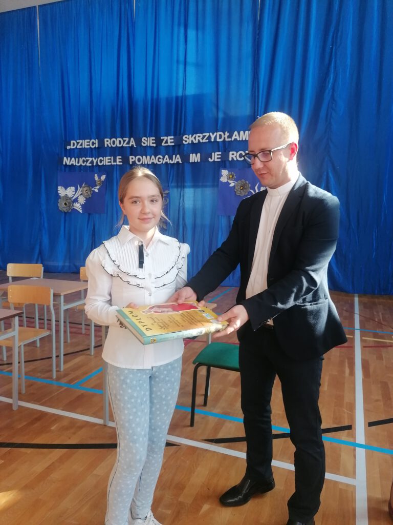 Ksiądz Łukasz wręcza nagrodę na 3-mce  w konkursie plastycznym o św. Jadwidze Śląskiej. 