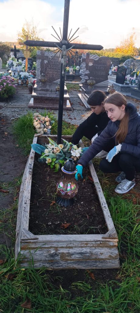 Akcja #Szkoła Pamięta- dziewczynki z kasy 6 b sprzątają zaniedbany grób. 