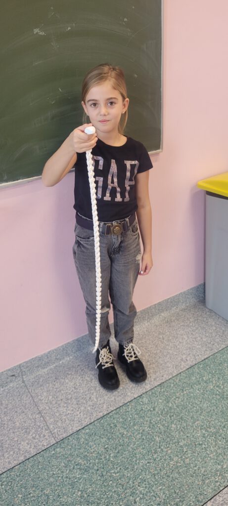 Uczennica trzyma w rączce biały ruchomy wąż wydrukowany na drukarce 3D. 