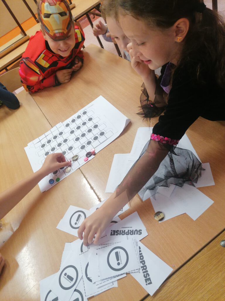 Wykorzystanie gry planszowej na zajęciach  dydaktyczno - wyrównawczych języka angielskiego, uczennica odkrywa kartę w celu wykonania zadania.
