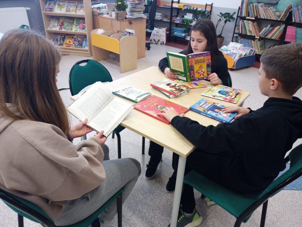 Odwiedziny uczniów pochodzących z Ukrainy w bibliotece szkolnej. Czytanie przez nich książek ufundowanych przez Fundację Powszechnego Czytania w ramach akcji "Książka chroni".
