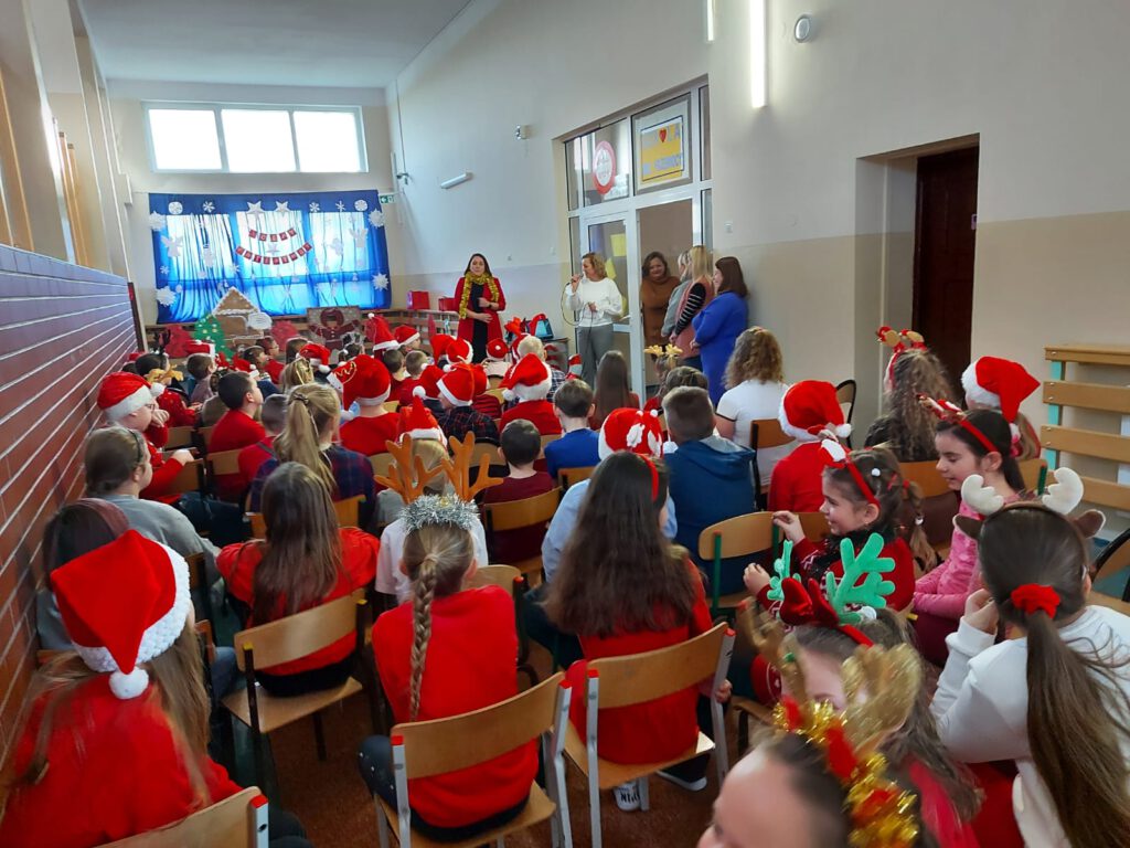 Koncert piosenek świąteczno- zimowych w języku angielskim. na zdjęciu widać uczniów klas 1-3 ubranych w świąteczne stroje. Pani Dyrektor przemawia do dzieci i składa im życzenia świąteczne. 