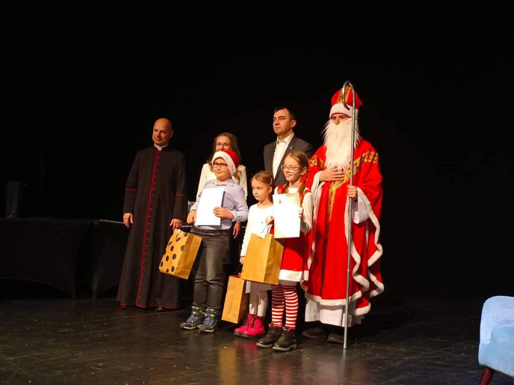 Na zdjęciu laureaci konkursu plastycznego ramach Dni ze Świętym Mikołajem pod hasłem "Święty Mikołaj biskup - patron Głogowa" stoją na scenie ze swoimi nagrodami i organizatorami konkursu. 