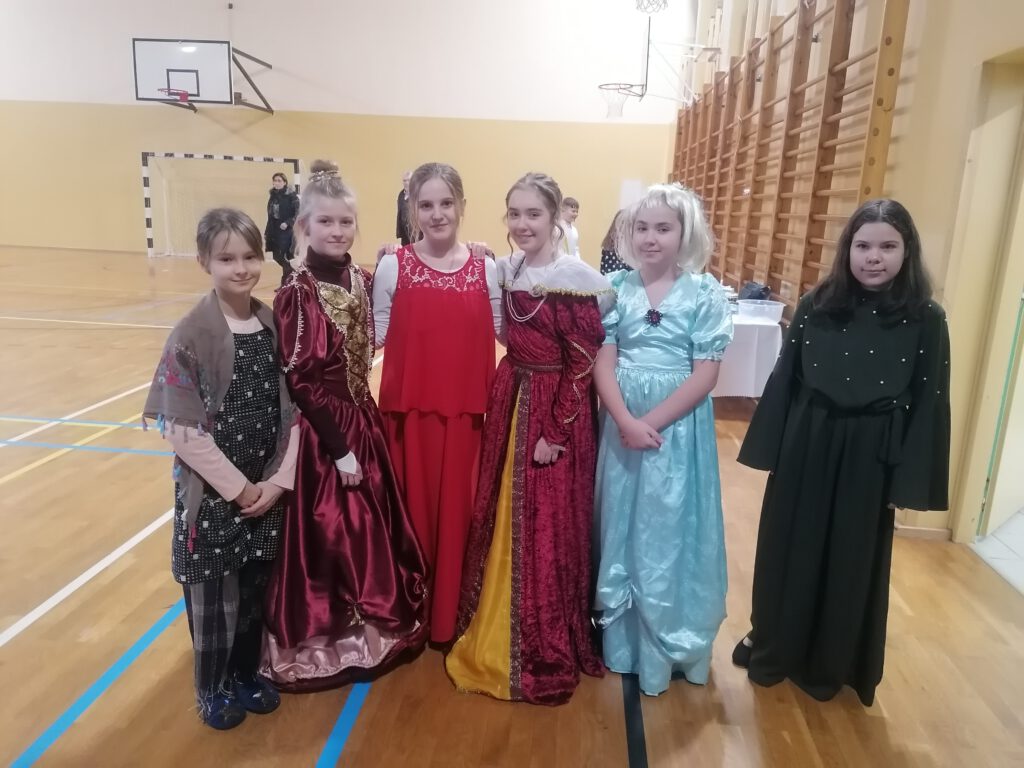 Na zdjęciu stoi sześć dziewczynek ubranych w suknie i inne stroje, które występują w przestawieniu szkolnym pt. "Kopciuszek".  