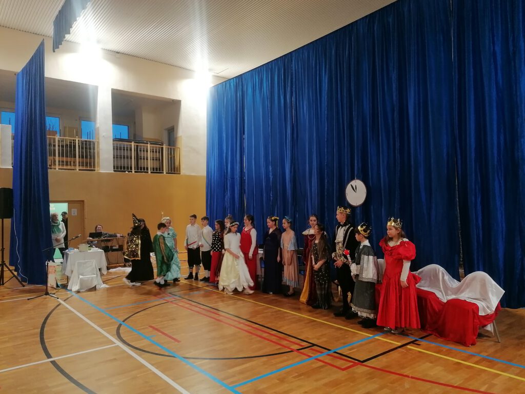 Zdjęcie przedstawia wszystkich uczniów klasy 4a, którzy brali udział w przedstawieniu "Kopciuszek". Uczniowie ubrani są w piękne i wytworne stroje. 