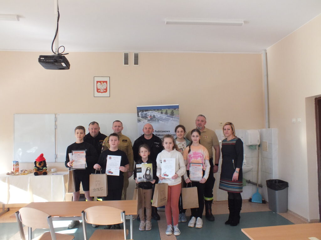 Zdjęcie przedstawia 6 uczniów ( dwóch chłopców i cztery dziewczynki) wraz z dyplomami i nagrodami za zajęte miejsca w konkursie. Na zdjęciu również pani Dyrektora  szkoły oraz czterech przedstawicieli straży, którzy pełnili funkcję jury. 