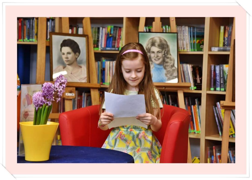 Zdjęcie przedstawia uczennicę  klasy pierwszej siedzącą na fotelu i czytającą wiersz w okazji "Wiosennego konkursu recytatorskiego dla uczniów klas 1-3"