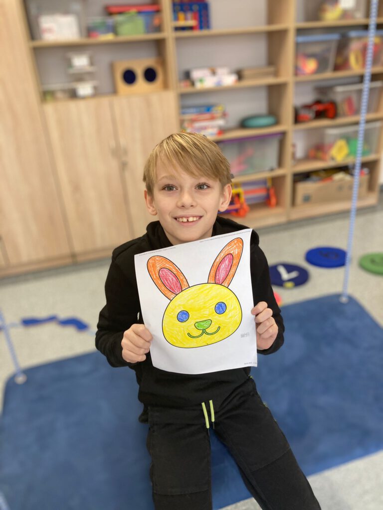 Uczeń trzyma w rękach swoją pracę pokolorowanego królika. 