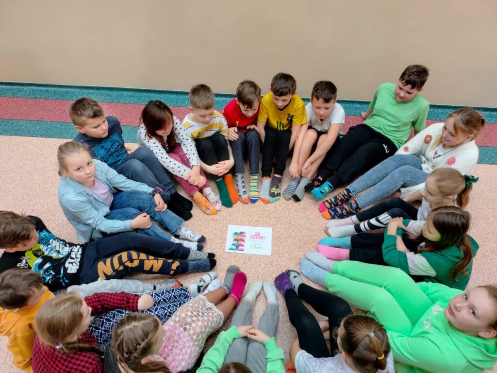 Na zdjęciu  uczniowie klasy 3 siedzą na podłodze i pokazują swoje kolorowe skarpetki.