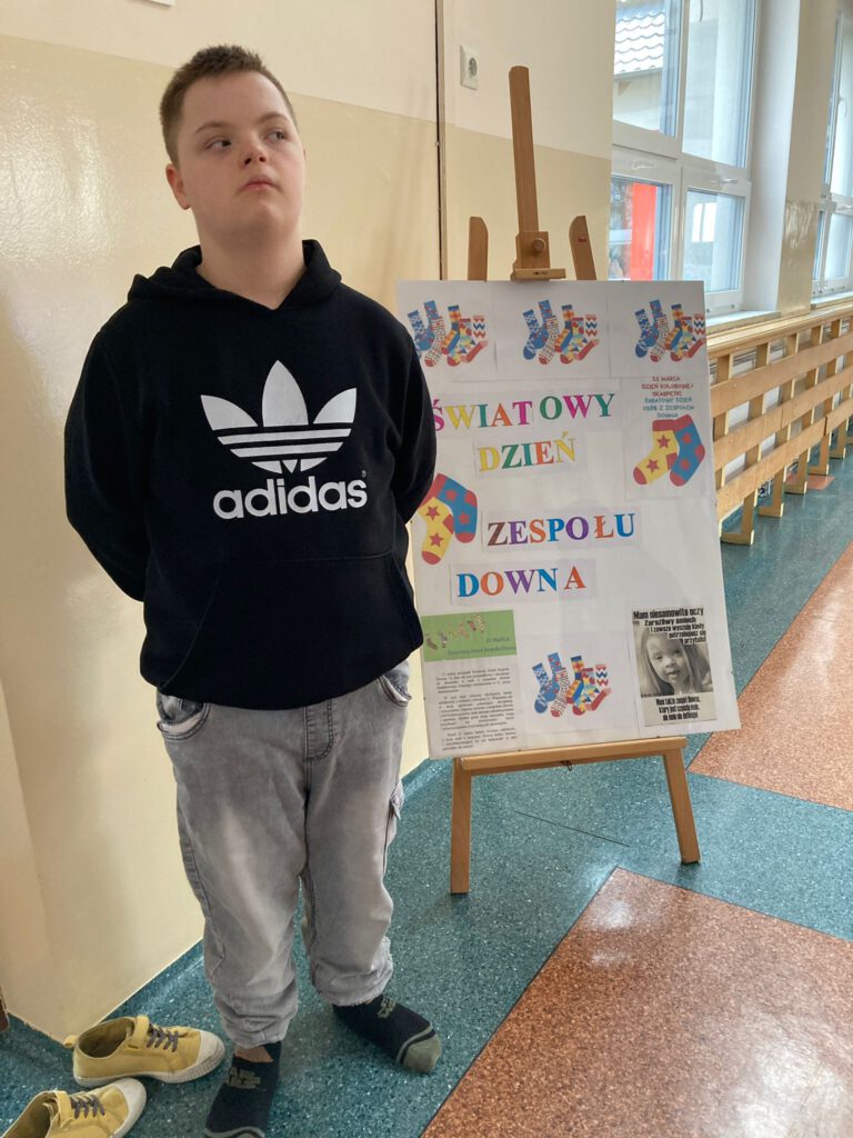 Na zdjęciu uczeń stoi obok plakatu na temat Dnia kolorowej skarpetki.