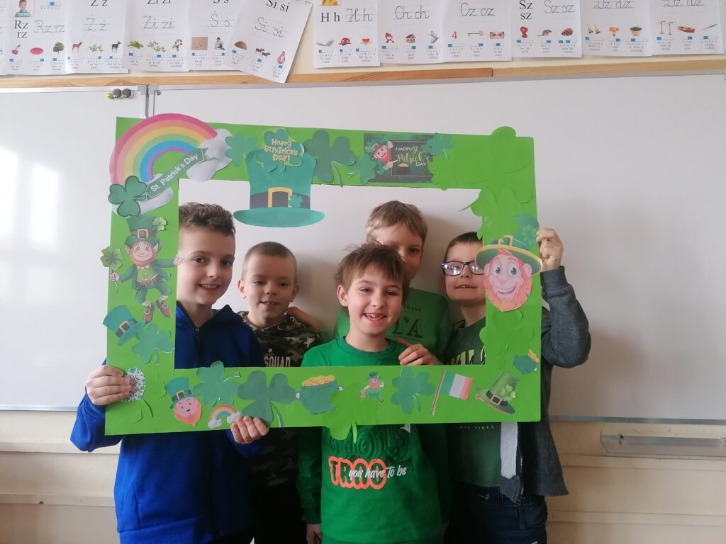 Obchody Dnia Świętego Patryka. Na zdjęciu stoi  5 chłopców, wokół ich  twarzy jest zielona ramka z symbolami Dnia św. Patryka. 