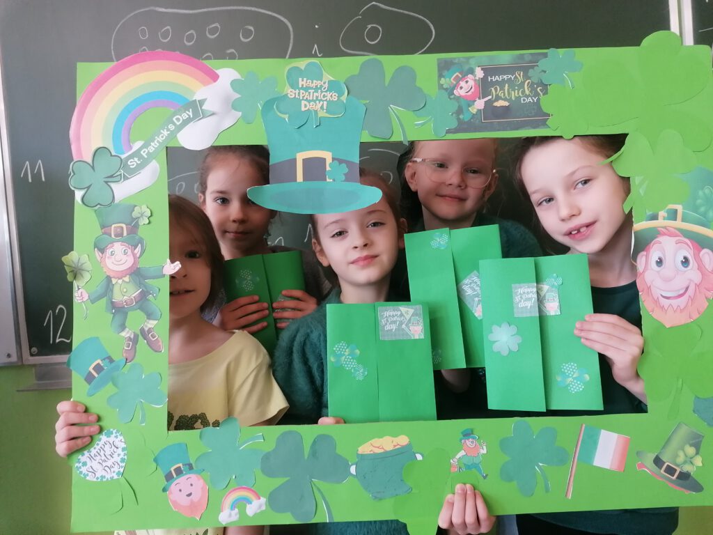 Obchody Dnia Świętego Patryka. Na zdjęciu znajdują się 4  dziewczynki, wokół ich  twarzy jest zielona ramka z symbolami Dnia św. Patryka. 