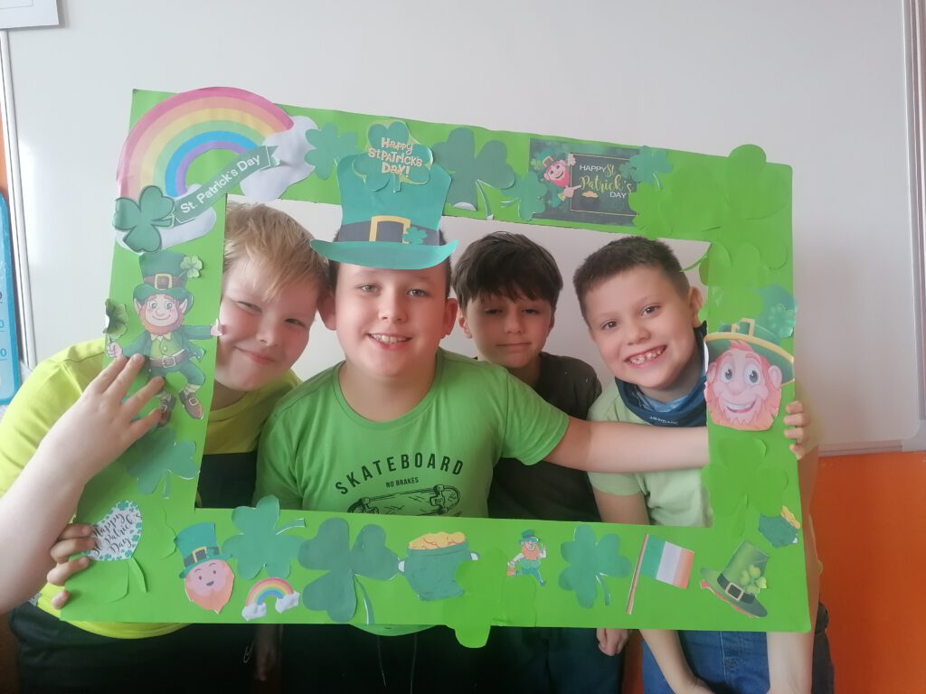 Obchody Dnia Świętego Patryka. Na zdjęciu stoi  4 chłopców, wokół ich  twarzy jest zielona ramka z symbolami Dnia św. Patryka. 