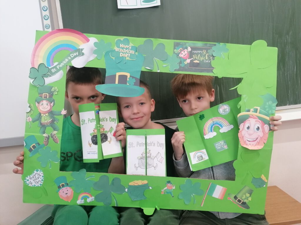 Obchody Dnia Świętego Patryka. Na zdjęciu siedzi 3 chłopców, wokół ich  twarzy jest zielona ramka z symbolami Dnia św. Patryka. 