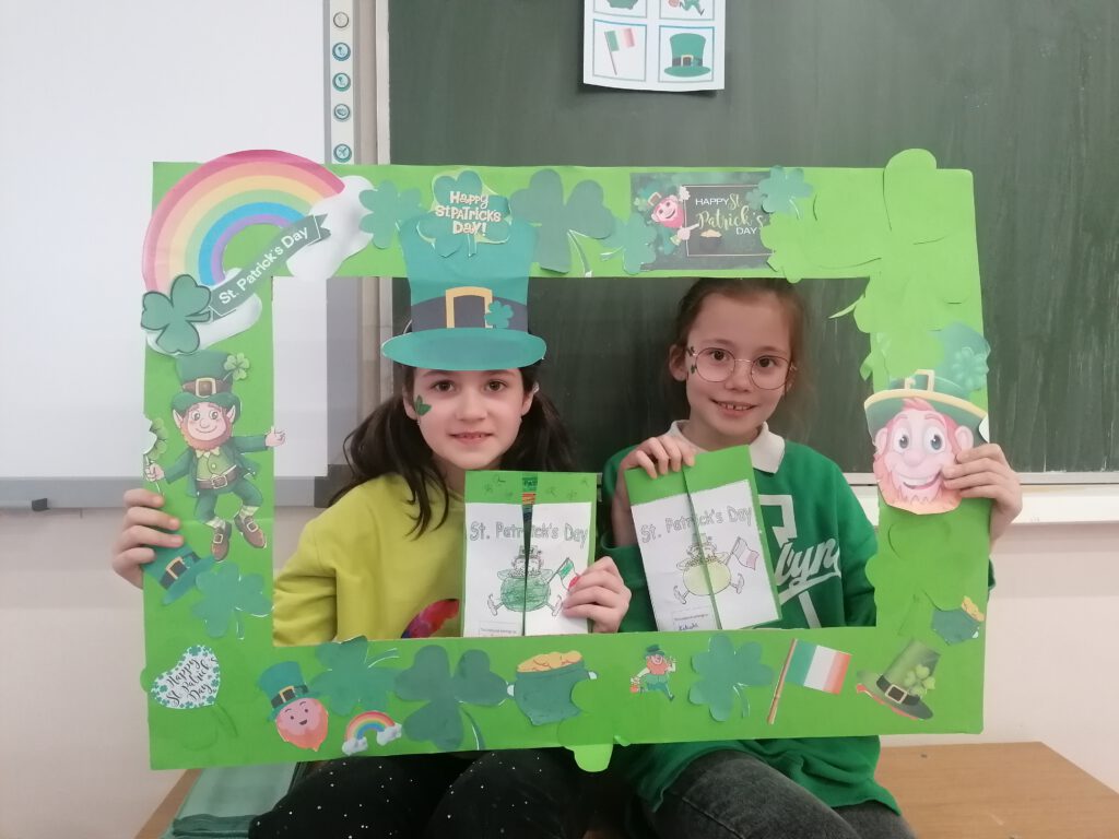 Obchody Dnia Świętego Patryka. Na zdjęciu siedzą dwie dziewczynki  wokół ich  twarzy jest zielona ramka z symbolami Dnia św. Patryka. 