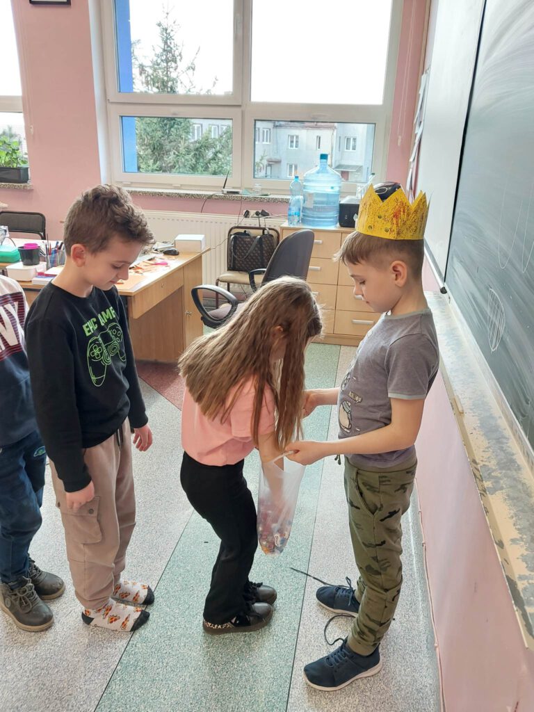 Zdjęcie przedstawia ucznia w koronie na głowie. Uczeń obchodzi swoje urodziny na świetliy i  częstuje innych uczniów cukierkami. 