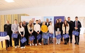 Powiatowe eliminacje Ogólnopolskiego  Turnieju Wiedzy Pożarniczej „Młodzież Zapobiega Pożarom”. Na zdjęciu stoją uczniowie, w ręce trzymają niebieskie torby 
 z nagrodami. 