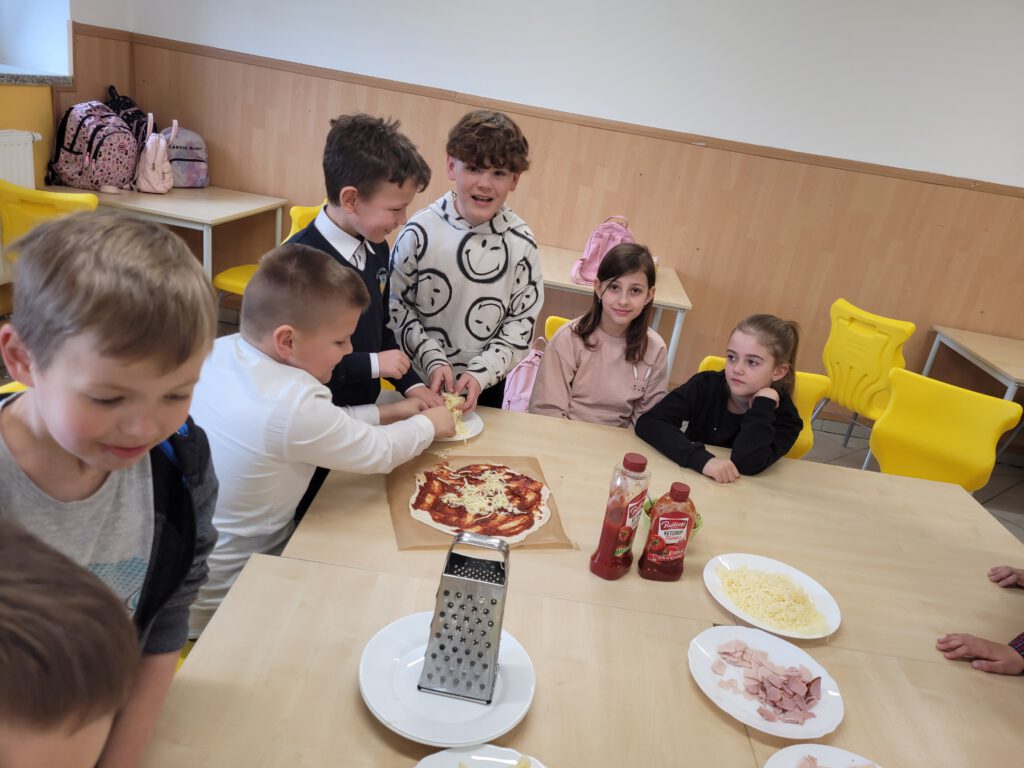 Pizza na zajęciach świetlicowych. Na zdjęciu czterech chłopców i dwie dziewczynki przygotowują swoją pizzę. 