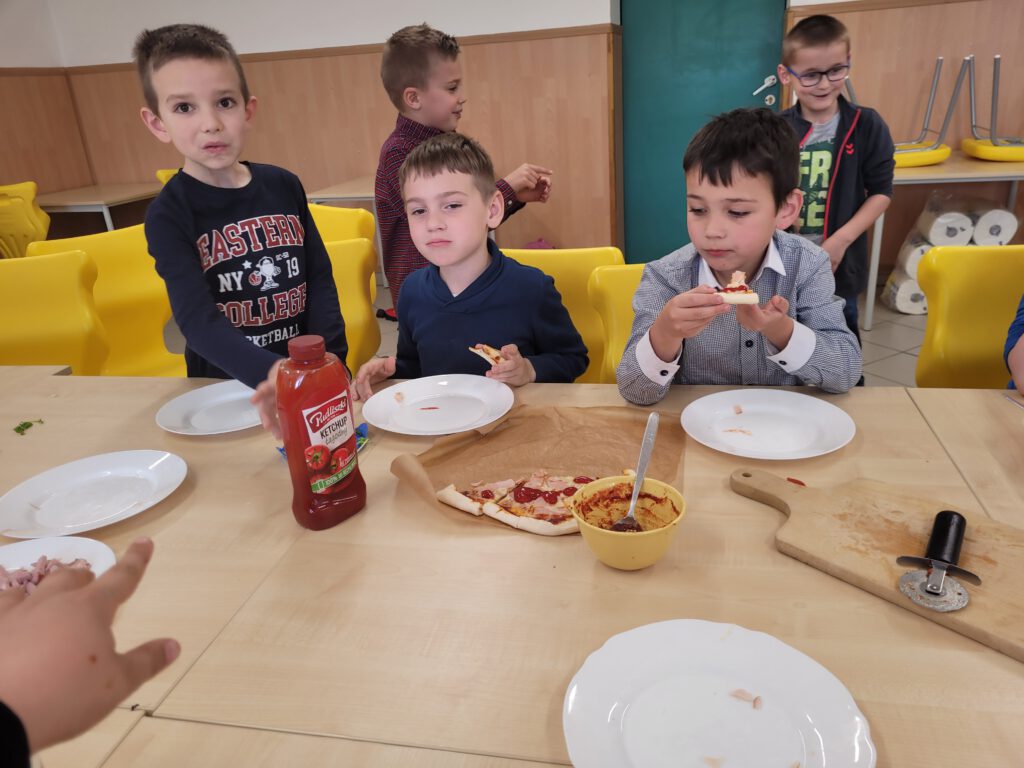 Pizza na zajęciach świetlicowych. Na zdjęciu chłopcy jedzą przygotowaną prze z siebie pizzę. 
