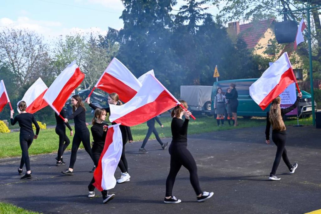 Obchody Majówki 2023. Na zdjęciu dziewczęta ubrane na czarno prezentują taniec trzymając w ręku biało-czerwoną flagę. 
