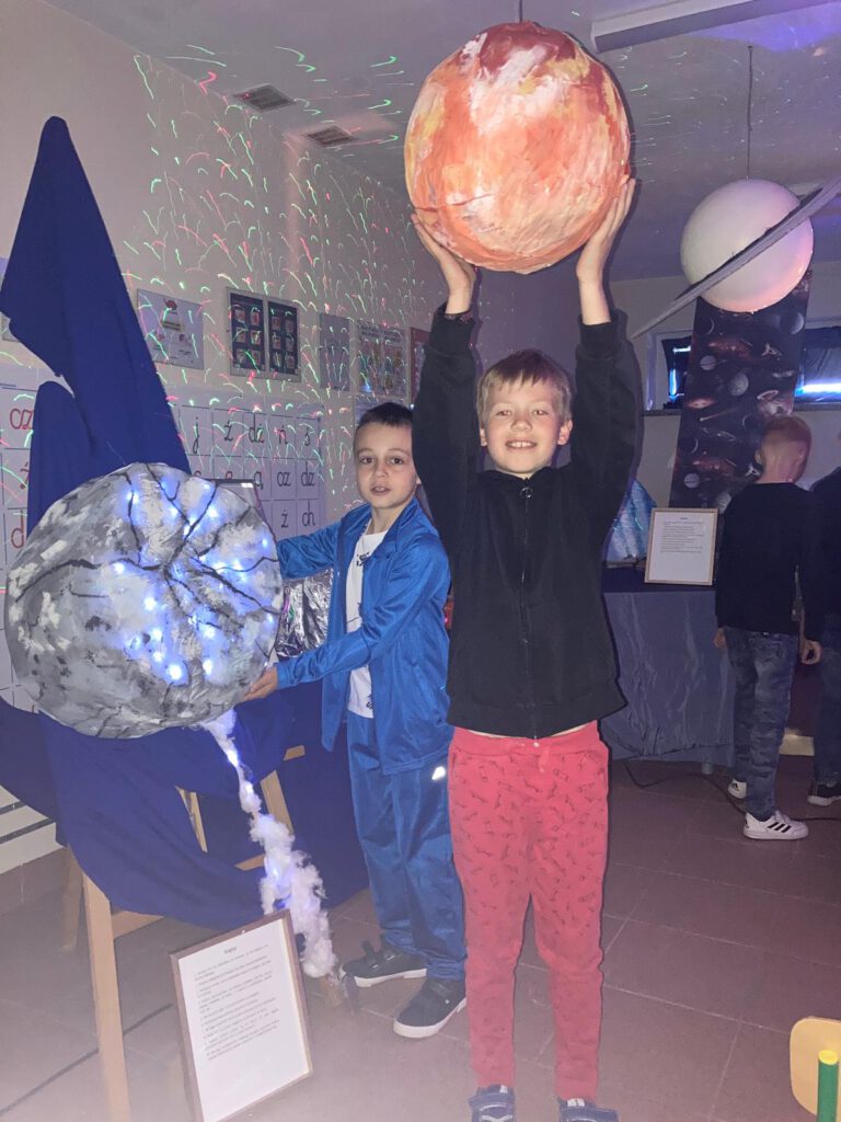 Szkolne obchody roku Mikołaja Kopernika. Na zdjęciu dwóch uczniów trzymających w rękach modele planet . 