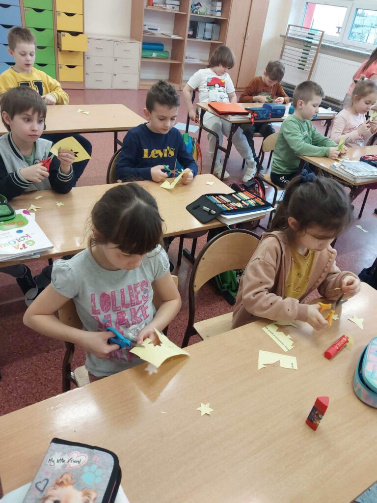 Akcja społeczno-edukacyjna "Żonkile". na zdjęciu uczniowie klasy pierwszej Wycinają z papieru elementy do złożenia żonkila z papieru. 