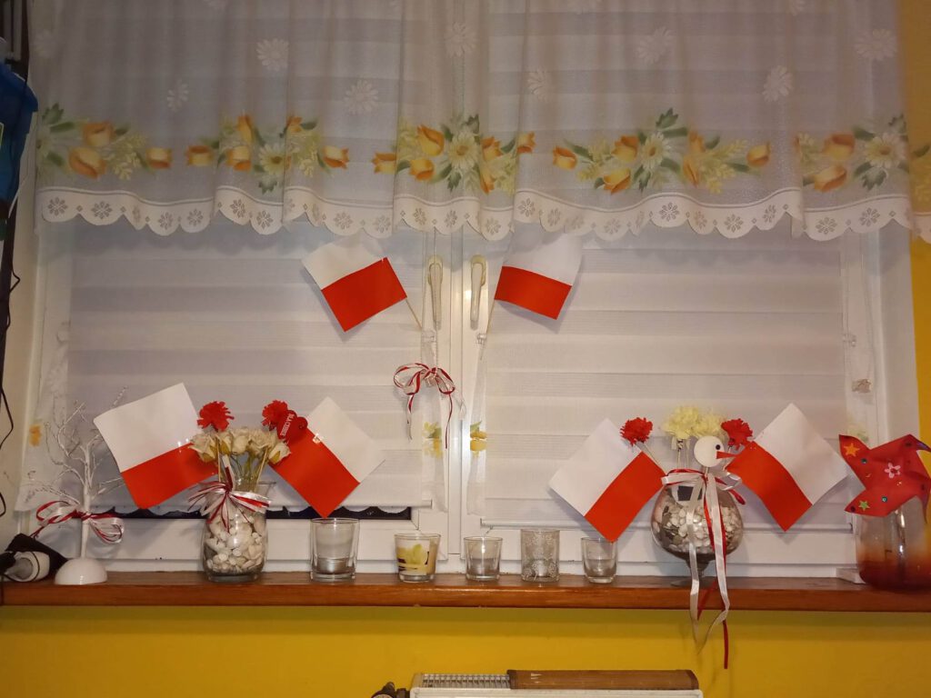 Szkolny konkurs "Majowe okienko". na zdjęciu okno przyozdobione biało- czerwonymi małymi flagami.