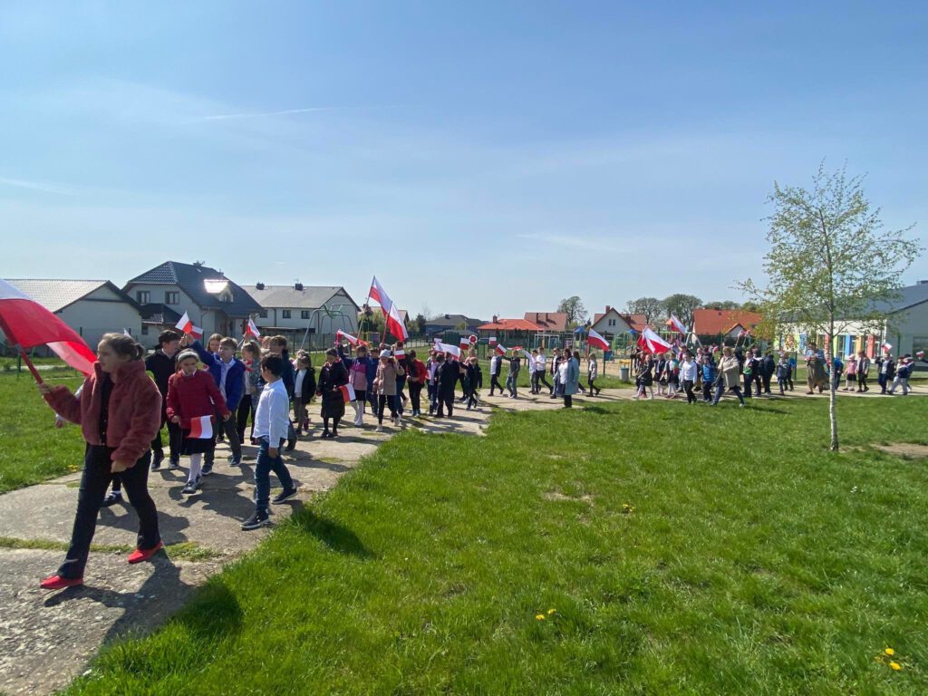 Spacer patriotyczny z okazji świat majowych. Na zdjęciu uczniowie uczestniczą w spacerze patriotycznym, w rękach trzymają flagi i chorągiewki biało-czerwone. 