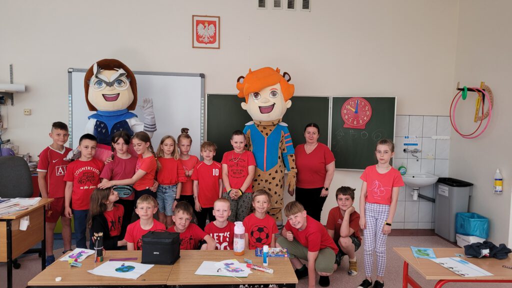 Międzynarodowy Dzień Dziecka na sportowo, zabawnie i kolorowo- „smaki z dzieciństwa-smaki świata- Chile”. Na zdjęciu uczniowie klasy 2 b, wraz z wychowawcą oraz festynowymi Maskotkami. Uczniowie ubrani są w czerwone koszulki. 
