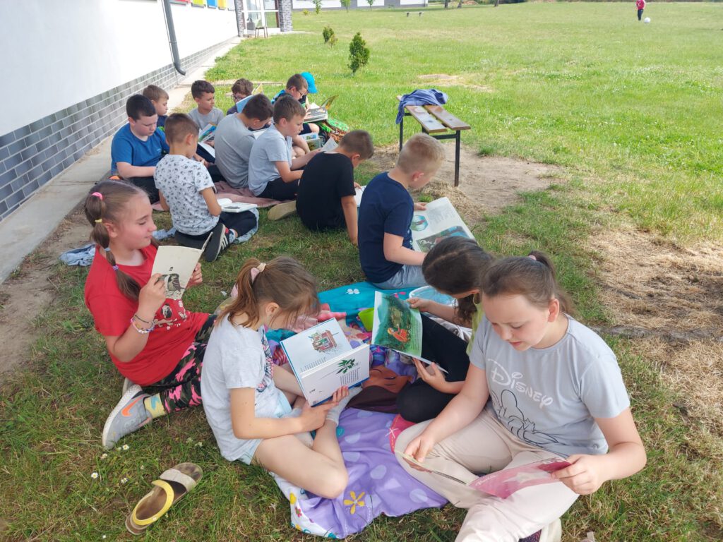 Akcja „Jak nie czytam, jak czytam. Starsi nie czytają? W młodych nadzieja”. Uczniowie siedzą na kocach i czytają książki na świeżym powietrzu.