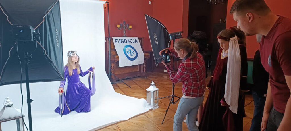 Podsumowanie projektu "Z Fundacją PZU po lekcjach". Na zdjęciu dziewczynka robiąca zdjęcie, obok fotograf, który udziela jej wskazówek.