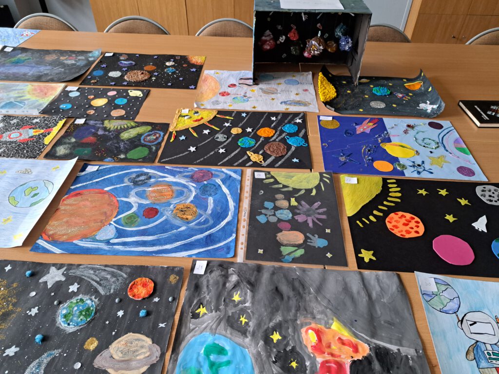 Zdjęcie przedstawia kolorowe prace konkursowe wykonane przez uczniów kl. 4b w ramach konkursu "Kosmos w moich oczach". Prace konkursowe wykonane zostały  różnych materiałów (planety z kaszy, ryżu; słońce z plasteliny).