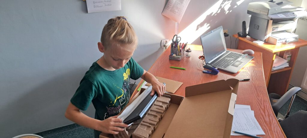 Rządowy program "Laptopy dla  ucznia". Na zdjęciu uczeń klasy czwartej rozpakowuje karton z laptopem. 