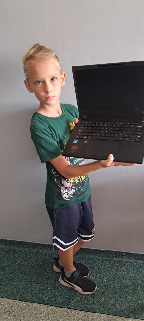 Rządowy program "Laptopy dla  ucznia". Na zdjęciu uczeń klasy 4 trzyma w rękach komputer. 
