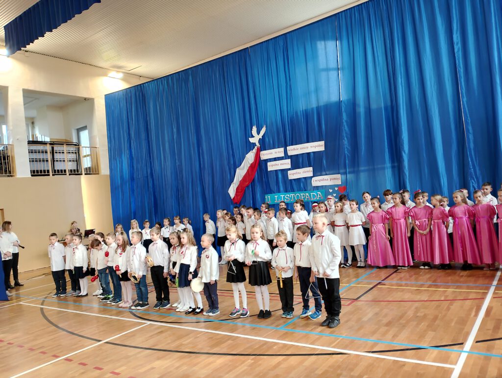Apel z okazji 11.listopada. Na zdjęciu uczniowie klas 1-3 ubrani w stroje galowe podczas prezentacji piosenki patriotycznej. 