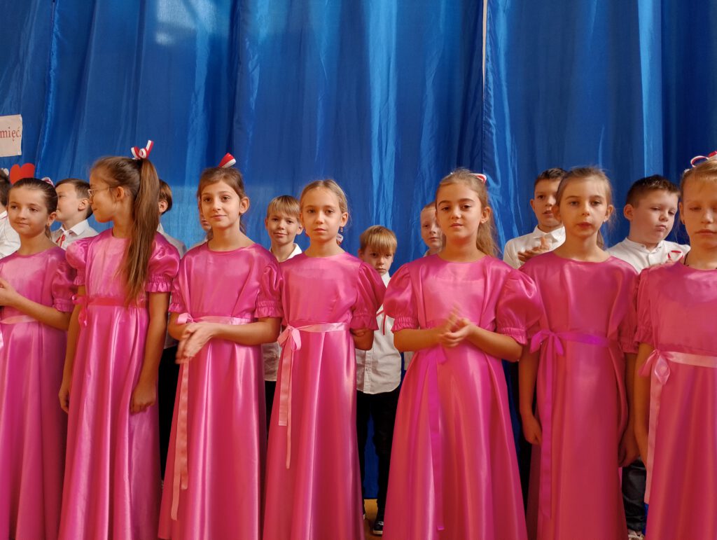 Apel z okazji 11.listopada. Na zdjęciu stoją dziewczynki ubrane w różowe sukienki, w których tańczyły poloneza, 