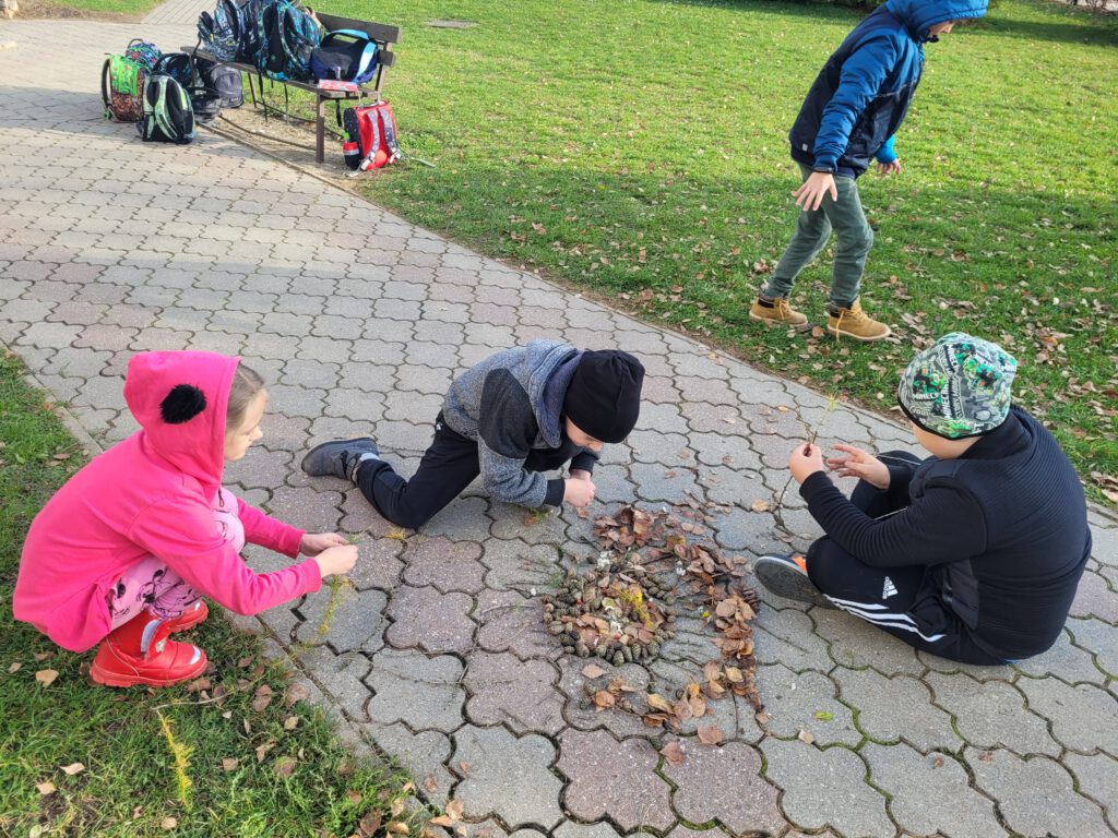 Uczniowie tworzą mandale na dworze z jesiennych skarbów.