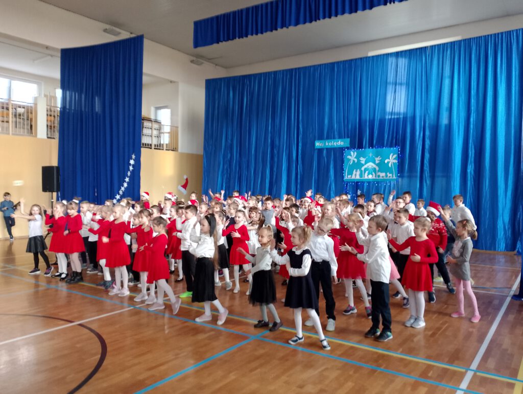 Apel świąteczny. Na zdjęciu wszyscy uczniowie edukacji wczesnoszkolnej wykonują układ taneczny i śpiewają piosenkę w języku angielskim. 