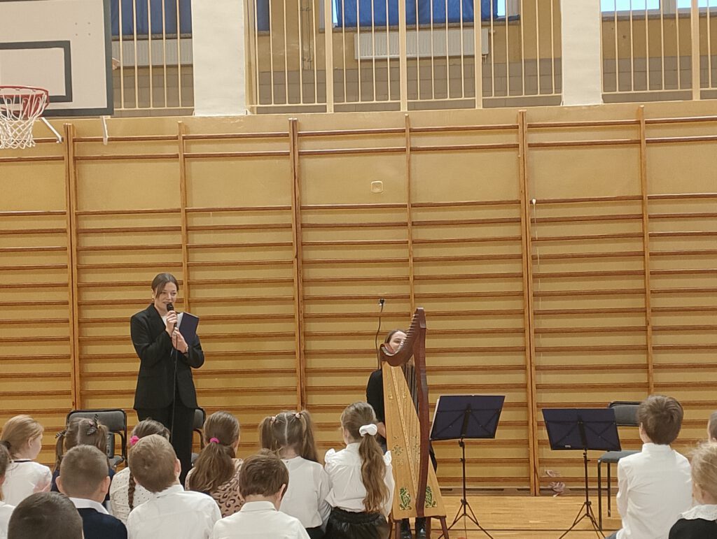 Koncert filharmonii- harfa i tuba. Na zdjęciu pani mówi do uczniów o harfie, obok siedzi pani z harfą. 