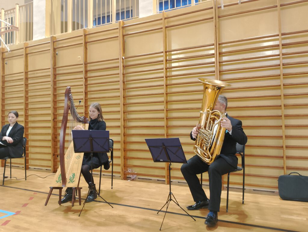 Koncert filharmonii- harfa i tuba. Na zdjęciu pan gra na tubie a pani na harfie. 