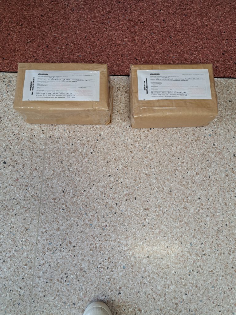 Zdjęcie przedstawia 2 kartony z groszami zapakowane w szary papier leżące na podłodze. 