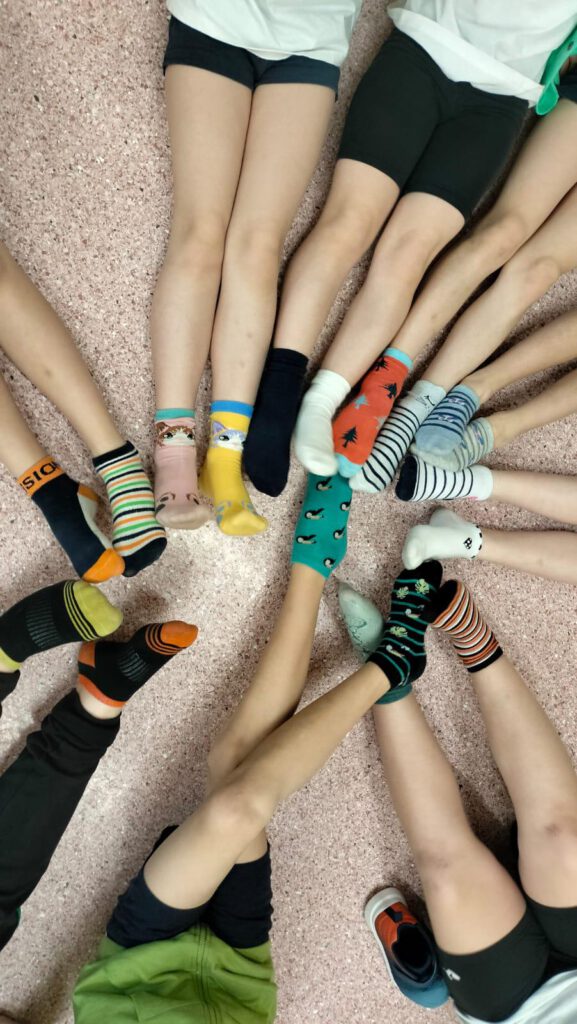 Dzień Kolorowej Skarpetki . Na zdjęciu  nogi uczniów z kolorowymi skarpetkami. 