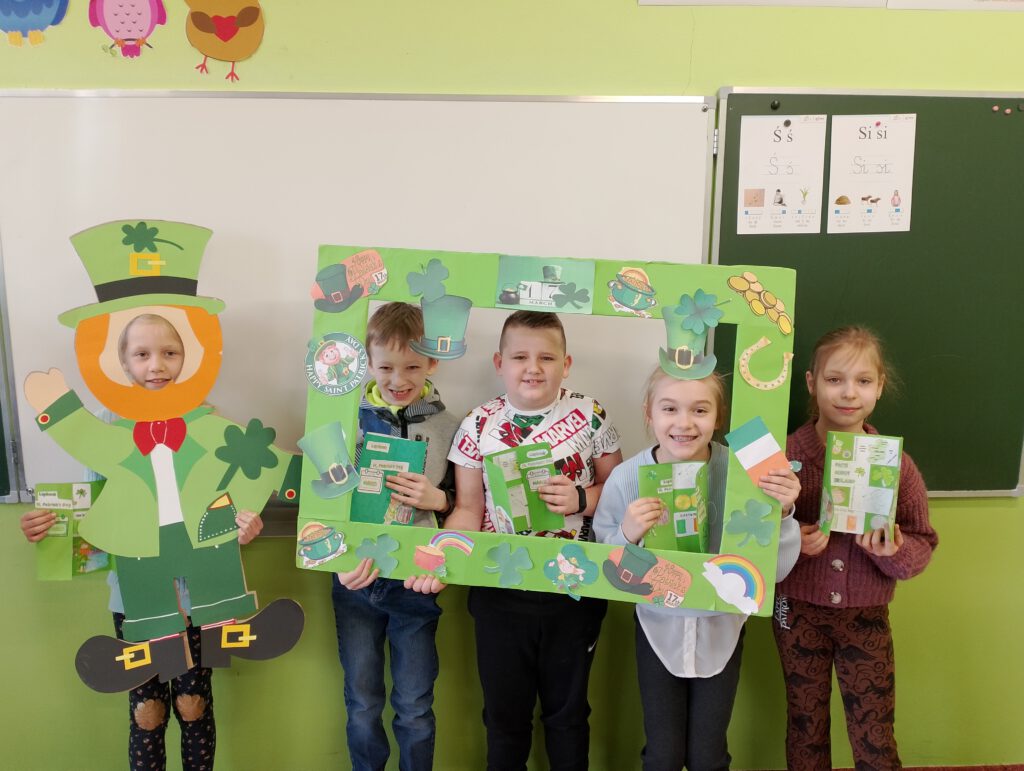 Obchody Dnia św. Patryka. Na zdjęciu uczniowie klasy pierwszej pozują do zdjęcia w zielonej fororamce i prezentują swoje lapbooki. 