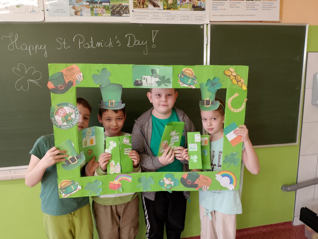 Obchody Dnia św. Patryka. Na zdjęciu uczniowie klasy drugiej pozują do zdjęcia w zielonej fotoramce. 