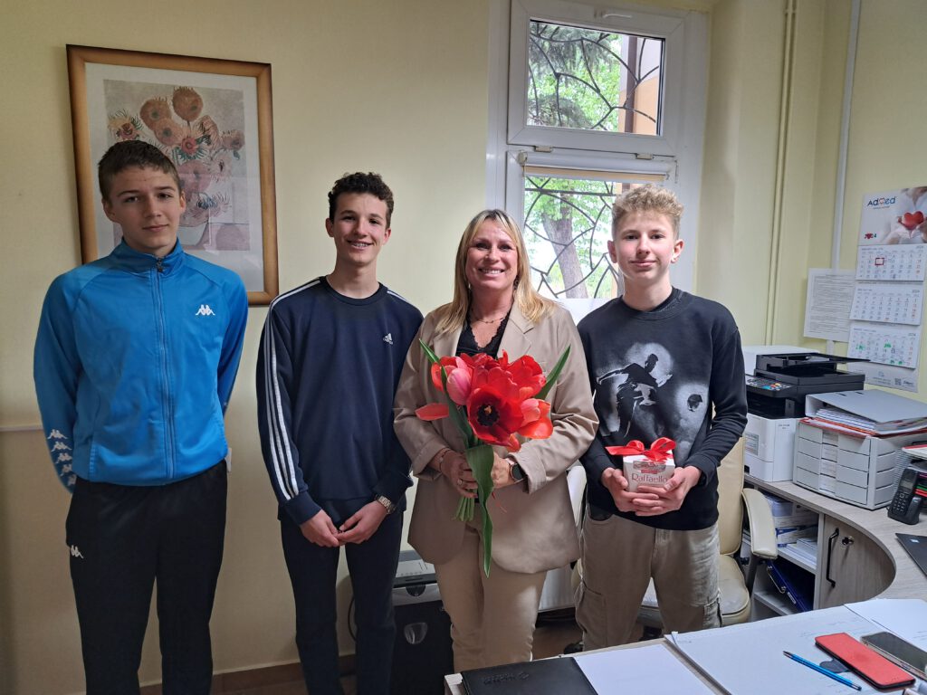 Przedstawia trzech uczniów wraz z p. Dyrektor Ośrodka Zdrowia w Gaworzycach. P. Dyrektor uśmiechnięta trzyma czerwone tulipany, jeden z uczniów Rafaello. W tle widać obraz wiszacy na ścian