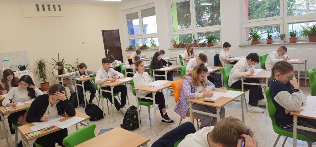 Kangur Matematyczny. Na zdjęciu uczniowie ubrani w strój galowy piszą konkurs Kangur Matematyczny. 