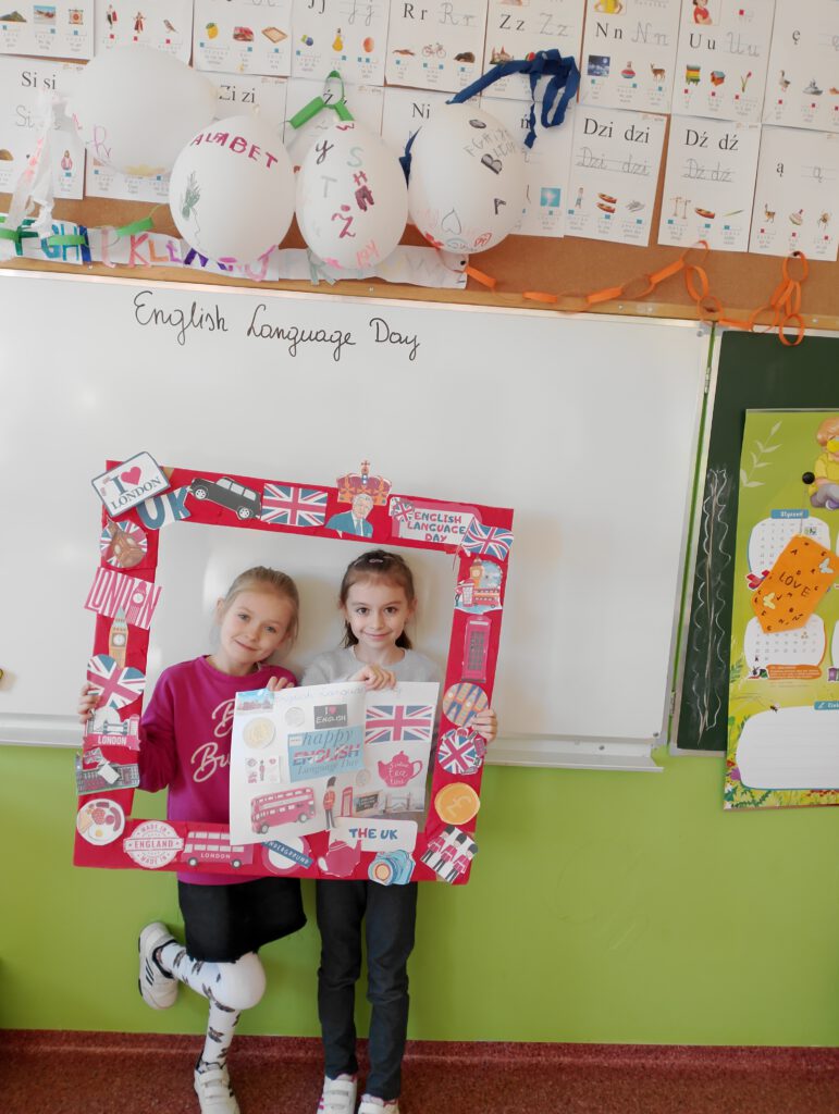 Dzień Języka Angielskiego. Na zdjęciu dwie dziewczynki pozują do zdjęcia  w foto ramce z elementami - symbolami Londynu i Wielkiej Brytanii. 