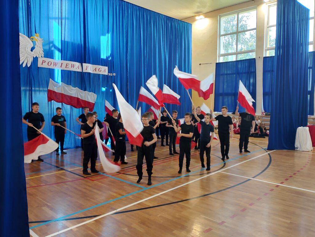 Apel z okazji świąt majowych. Na zdjęciu chłopcy ubrani na czarno wykonują taniec z uniesionymi biało-czerwonymi flagami. 
