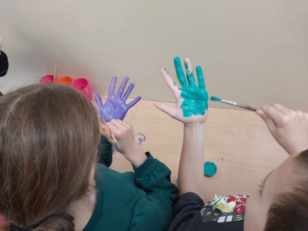 Plakaty pt. "Ziemia w Twoich rękach". Uczniowie malując ręce farbami  przygotowują je do odbicia na plakacie. 